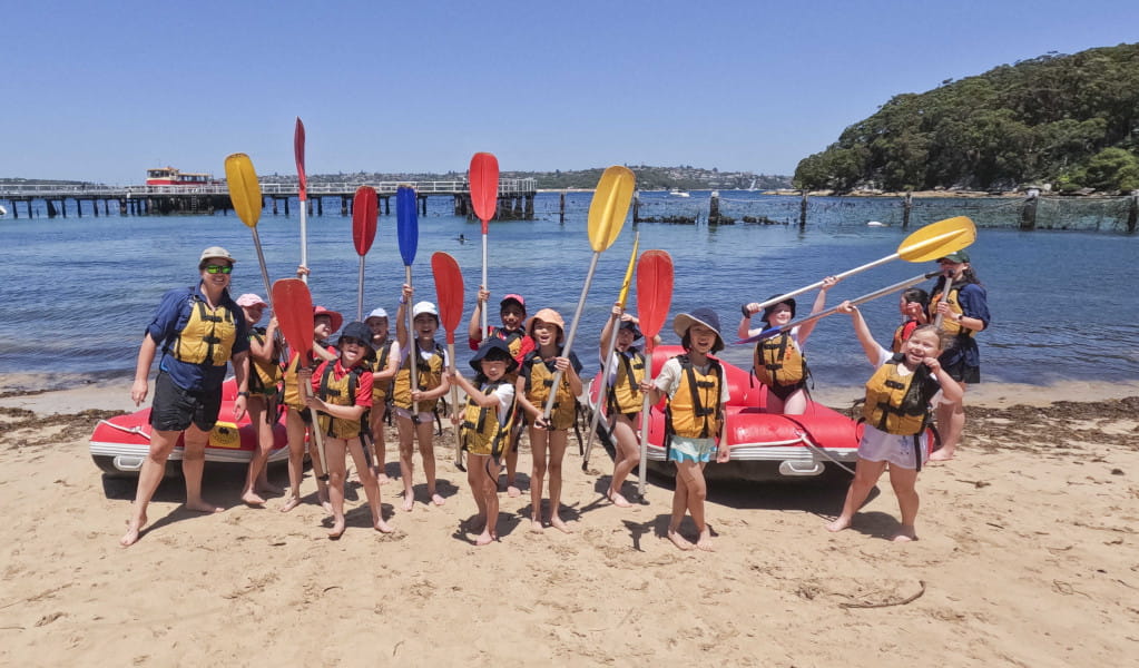 Group of children wearing lifejackets and holding paddles pose for photo on beach. Photo: &copy; Lands Edge Foundation Saltwater School