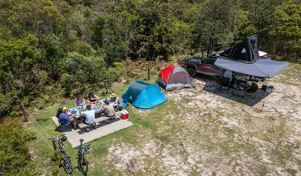 A group of campers eating at the picnic table on their campsite at Mibanbah-Black Rocks campground. Credit: John Spencer &copy; DCCEEW