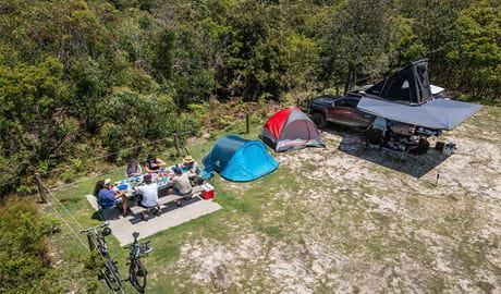 A group of campers eating at the picnic table on their campsite at Mibanbah-Black Rocks campground. Credit: John Spencer &copy; DCCEEW