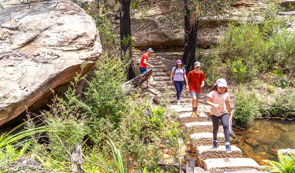 2 kids and 2 adults rock hopping across Marrangaroo Creek along Lost City walking track in Gardens of Stone State Conservation Area. Credit: Simone Cottrell &copy; DCCEEW