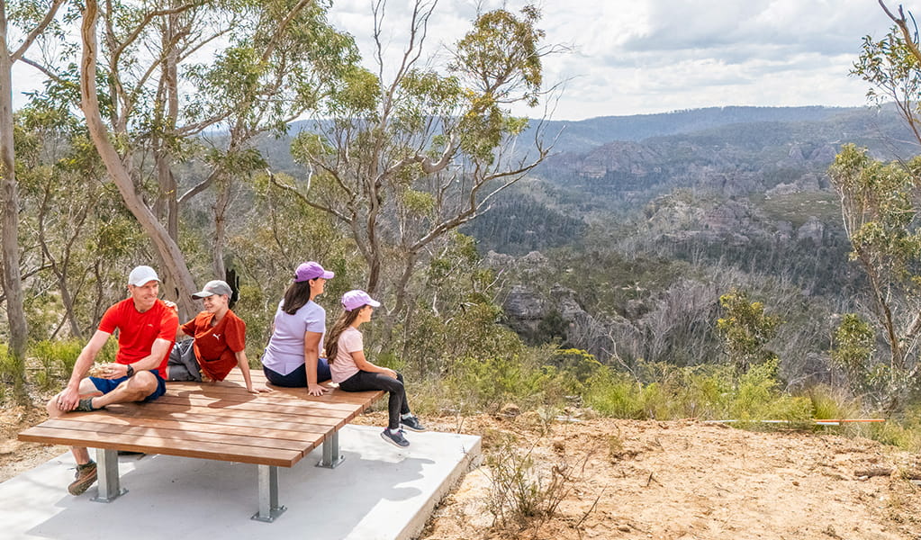 2 adults and 2 kids sitting at a square platform bench at Lost City Lookout, Gardens of Stone State Conservation Area near Lithgow. Credit: Simone Cottrell &copy; DCCEEW