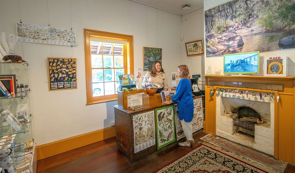 A visitor talking to a Hartley Historic Site Visitor Centre staff member at the counter beside an old fireplace. Credit: John Spencer &copy; DCCEEW