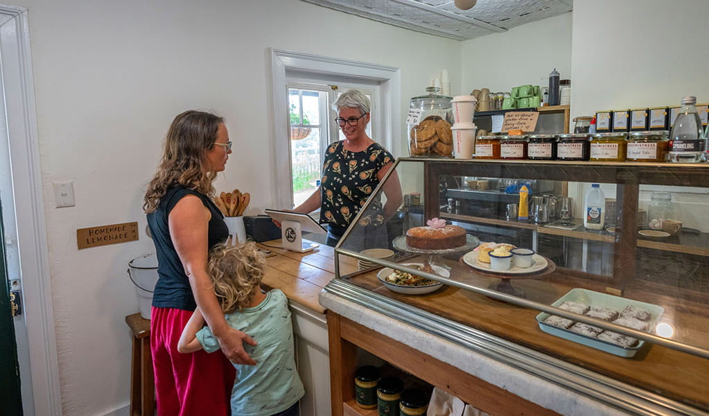 A woman and child at the counter inside The Postmistress Cafe and Store next to a pastry display. Credit: John Spencer &copy; DCCEEW