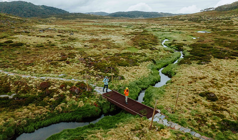 2 hikers crossing a creek between Charlotte Pass Village and Perisher Valley in Kosciuszko National Park. Credit: Daniel Parsons / DCCEEW © Caravel Content