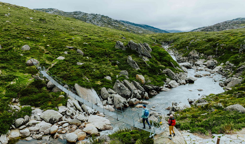 2 bushwalkers crossing a creek along Illawong walk in the Thredbo-Perisher area of Kosciuszko National Park. Credit: Daniel Parsons / DCCEEW &copy; Caravel Content