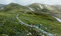 2 hikers on a track along Main Range walk with a view of snow-capped mountains and a lake in the background. Credit: Daniel Parsons / DCCEEW &copy; Caravel Content