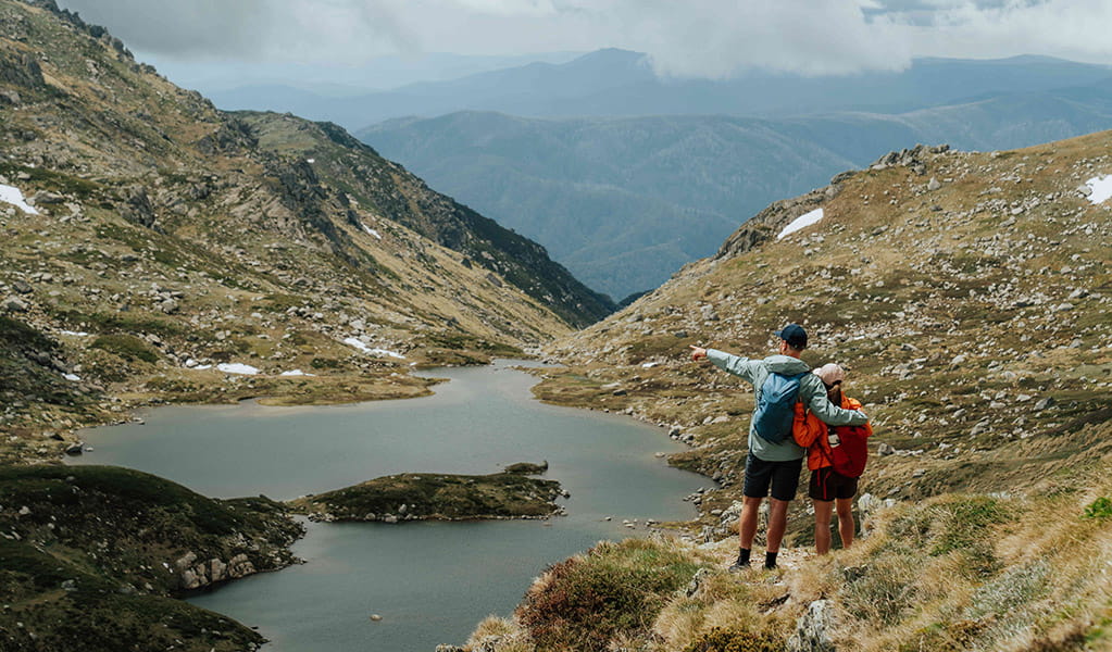 2 hikers on a track along Main Range walk with admiring the view of a lake. Credit: Remy Brand / DCCEEW © Caravel Content