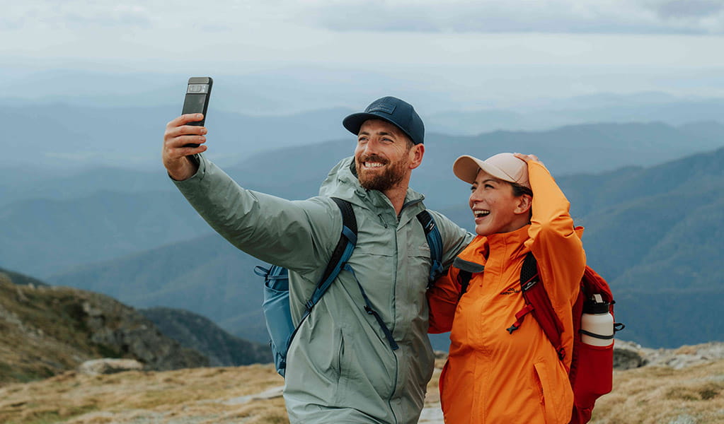 A man and woman taking a selfie at the summit of Mount Kosciuszko in the Thredbo-Perisher area. Credit: Remy Brand / DCCEEW &copy; Caravel Content