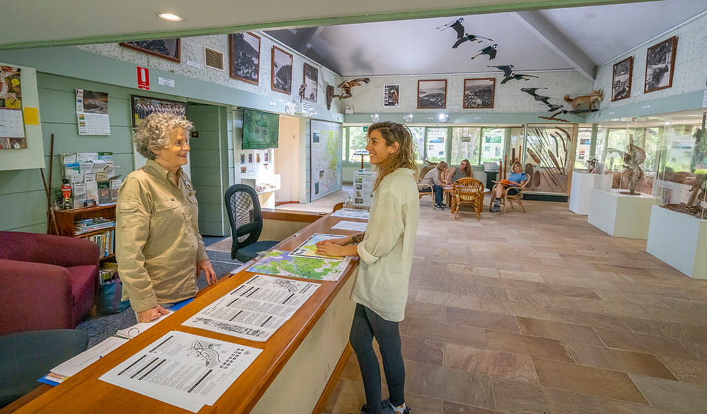 A visitor stands at the info desk talking to a volunteer at Kalkari Discovery Centre, Ku-ring-gai Chase National Park. Photo: Johny Spencer &copy; DCCEEW