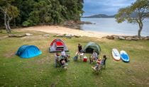 A group of campers sitting near their tents by the beach and bush at The Basin campground. Credit: John Spencer/DCCEEW &copy; DCCEEW