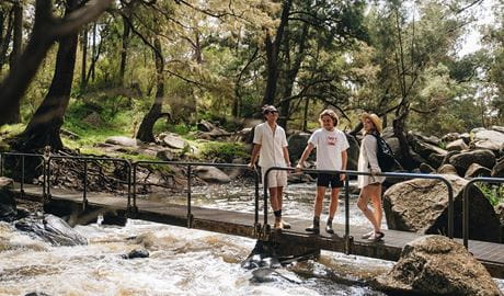 Three friends stand on a small bridge over a fast-flowing river near Blue Hole picnic area. Credit: Harrison Candlin/DCCEEW  &copy; Armidale Regional Council 