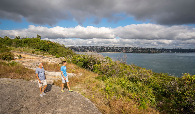 Two people walking along the rocks at Middle Head – Gubbuh Gubbuh in Sydney Harbour National Park. Photo: John Spencer, &copy; DCCEEW