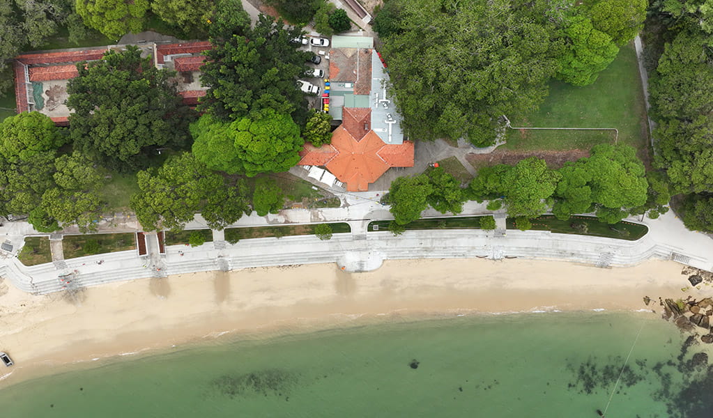 Aerial photo of Shark Beach at Nielsen Park showing the ocean and a concrete seawall bordering lush green parkland and the pavillion. Credit: Drew Elliott/DCCEEW &copy; DCCEEW 