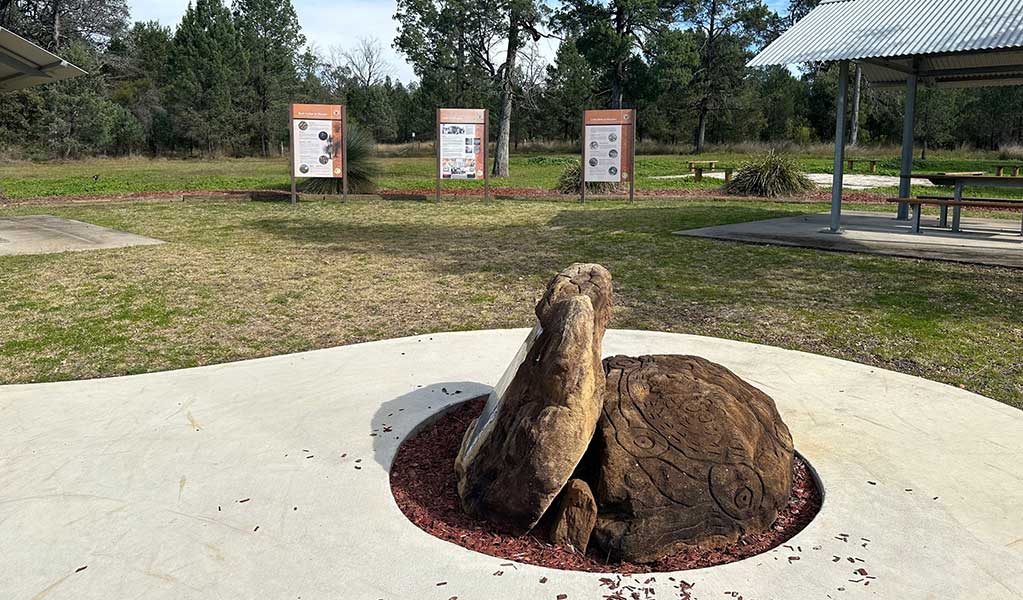 A rock with Aboriginal engravings with information signs and shelters for Terry Hie Hie Aboriginal area in the background. Credit: DCCEEW &copy; DCCEEW