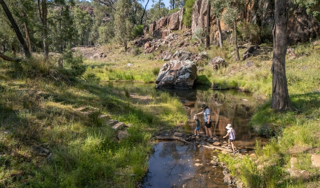 A family rock-hopping across Wambelong Creek on Wambelong Nature walking track in Warrumbungle National Park. Photo: John Spencer &copy; DCCEEW