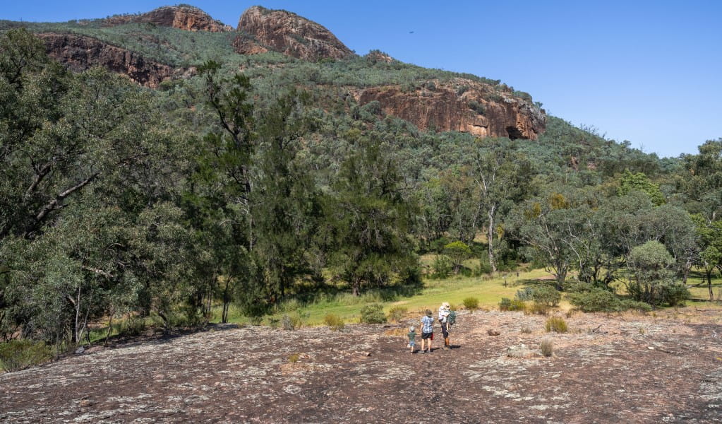 A family walking across a rock platform with views of mountains in the distance on Wambelong Nature walking track in Warrumbungle National Park. Photo: John Spencer &copy; DCCEEW