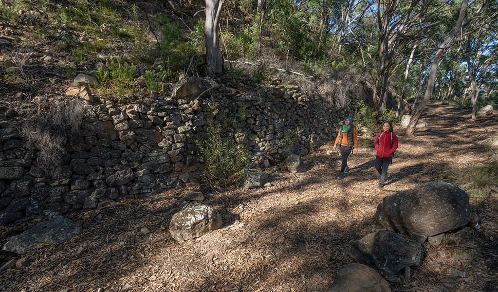 2 hikers passing stone wall remnants of old train infrastructure on the Glow Work Tunnel via Wolgan Valley loop. Credit: John Spencer &copy; DCCEEW