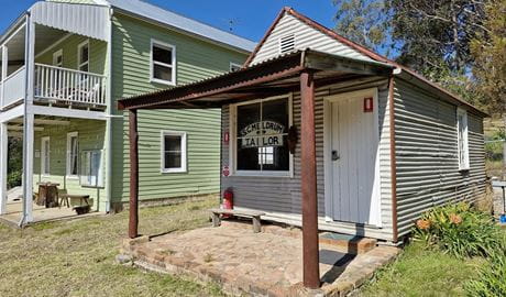 The Tailors Room is a small grey wooden cabin, with a white front door and large white-framed front window, Yerranderie Regional Park. Photo: Hassan Elbatoory &copy;DCCEEW